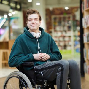 Young student with earphones in a wheelchair - with library in the background